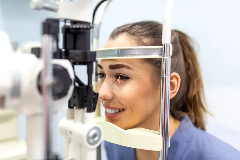 A patient resting her chin on a slit lamp during an eye examination, the instrument’s light crossing her eye.